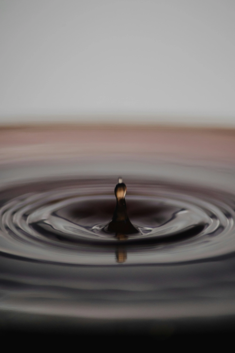 CLARI³ - Coaching - Ein Wassertropfen erzeugt Wellen auf einer ruhigen, dunklen Oberfläche.
