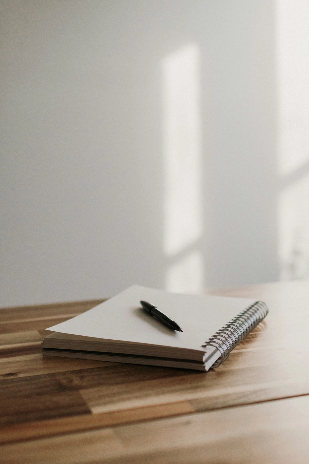 CLARI³ - Coaching - Ein leeres Spiralnotizbuch und ein Stift auf einem Holztisch.